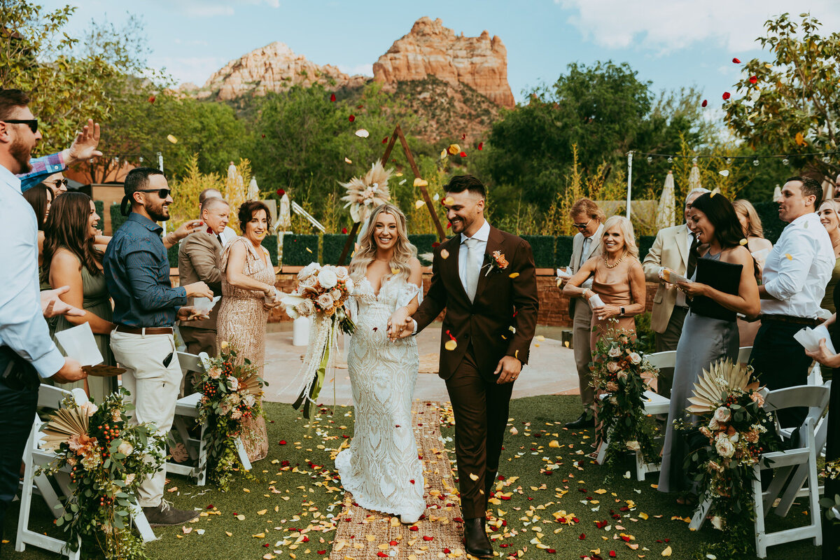 couple smiling with rose petals being thrown down wedding isle at amara resort in sedona