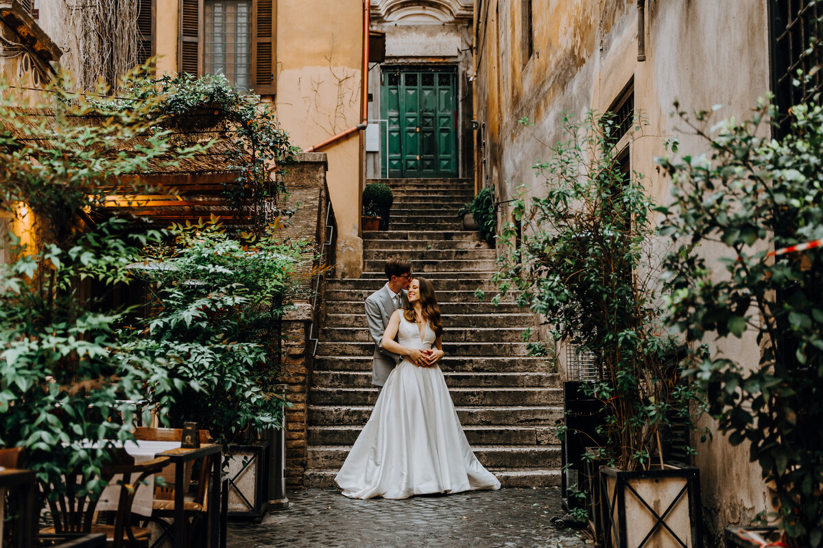 Couple standing on stone staircase in narrow Roman alley.