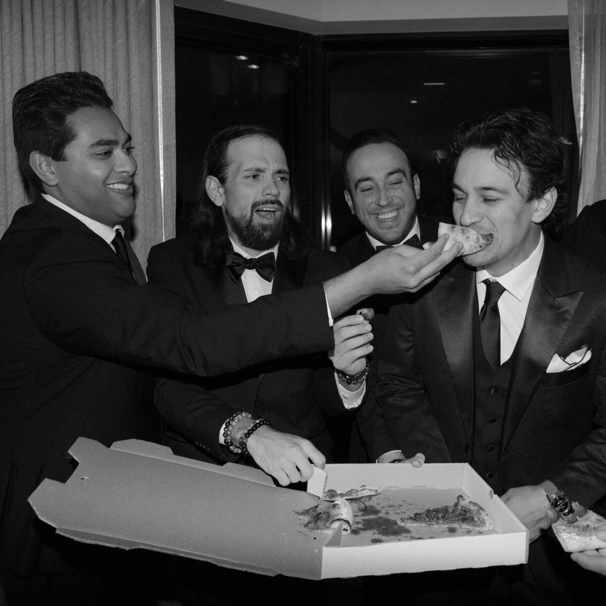 A group of men eating pizza in their black wedding suits