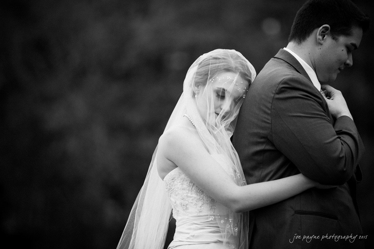 A bride hugging a groom from behind.