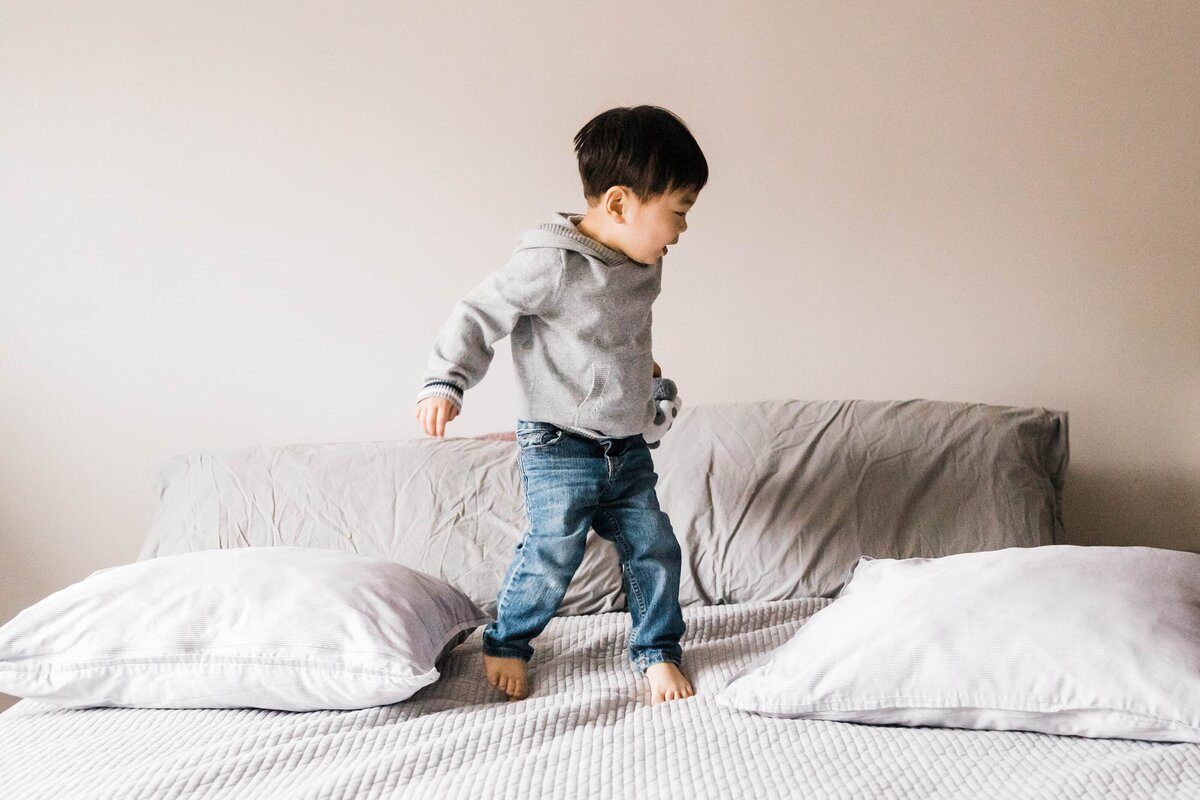 Family photographer in Pittsburgh captures toddler walking across bed with pillows.
