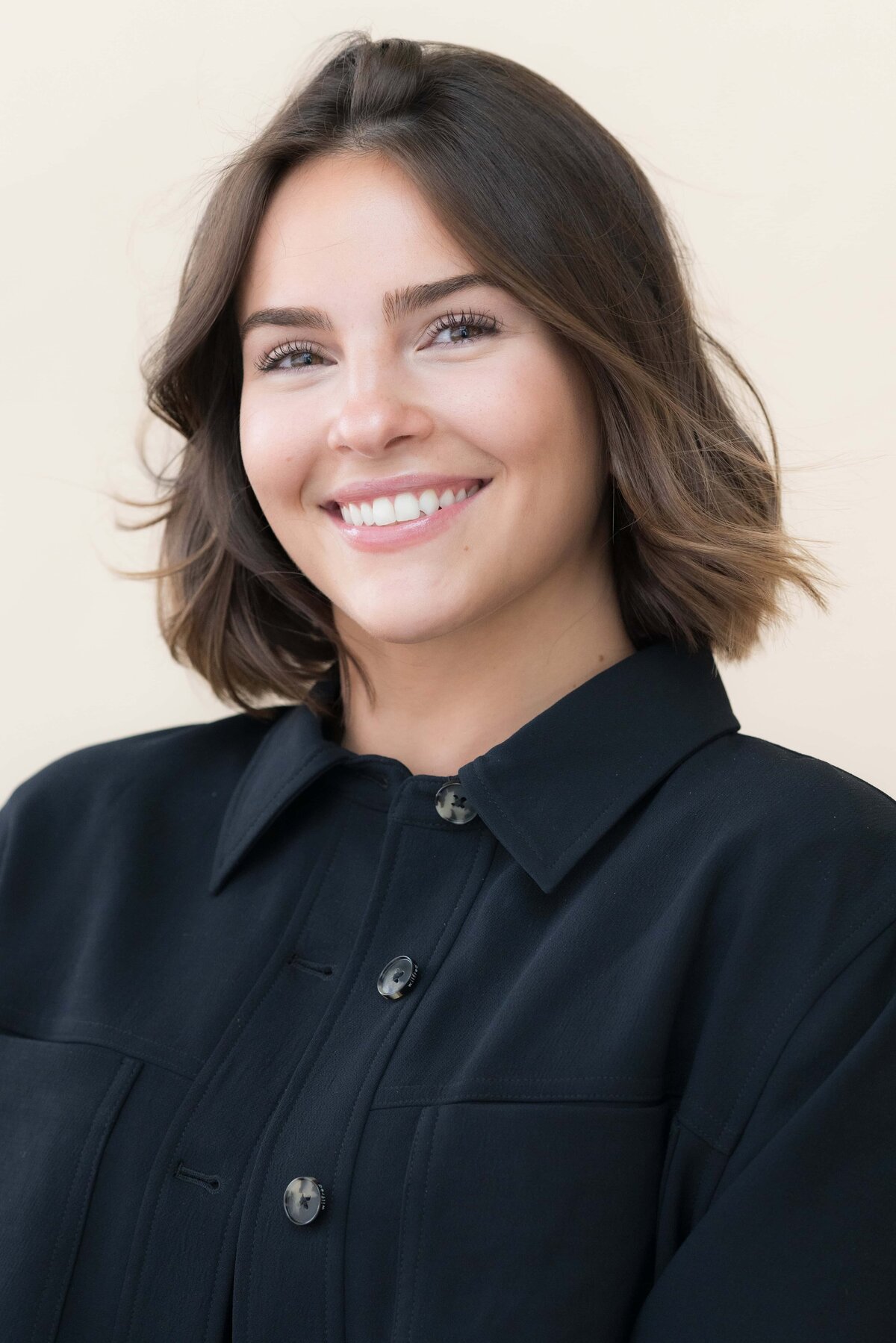 young woman with dark hair smiling while wearing a dark shirt posed for a professional headshot