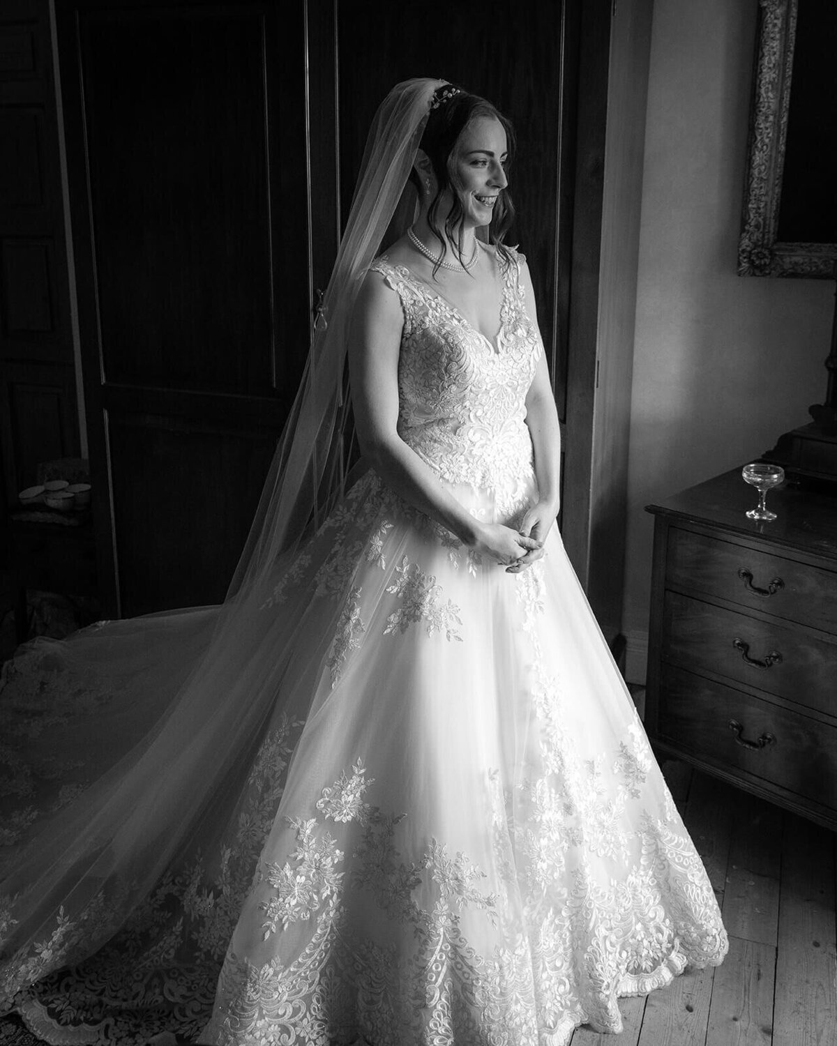 A bride looks towards a window standing up in a long wedding dress with a cathedral veil