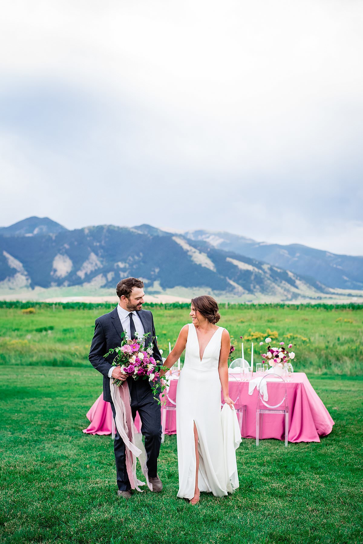 Couple standing together in vibrant green field with pink bouquet and Montana mountains in the background