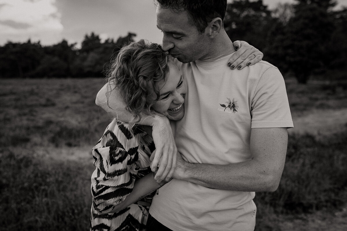 Verliefd stel man heeft arm om vrouw heen geslagen en kust haar op haar slaap en vrouw heeft ook arm om man heen op de heide zwartwit