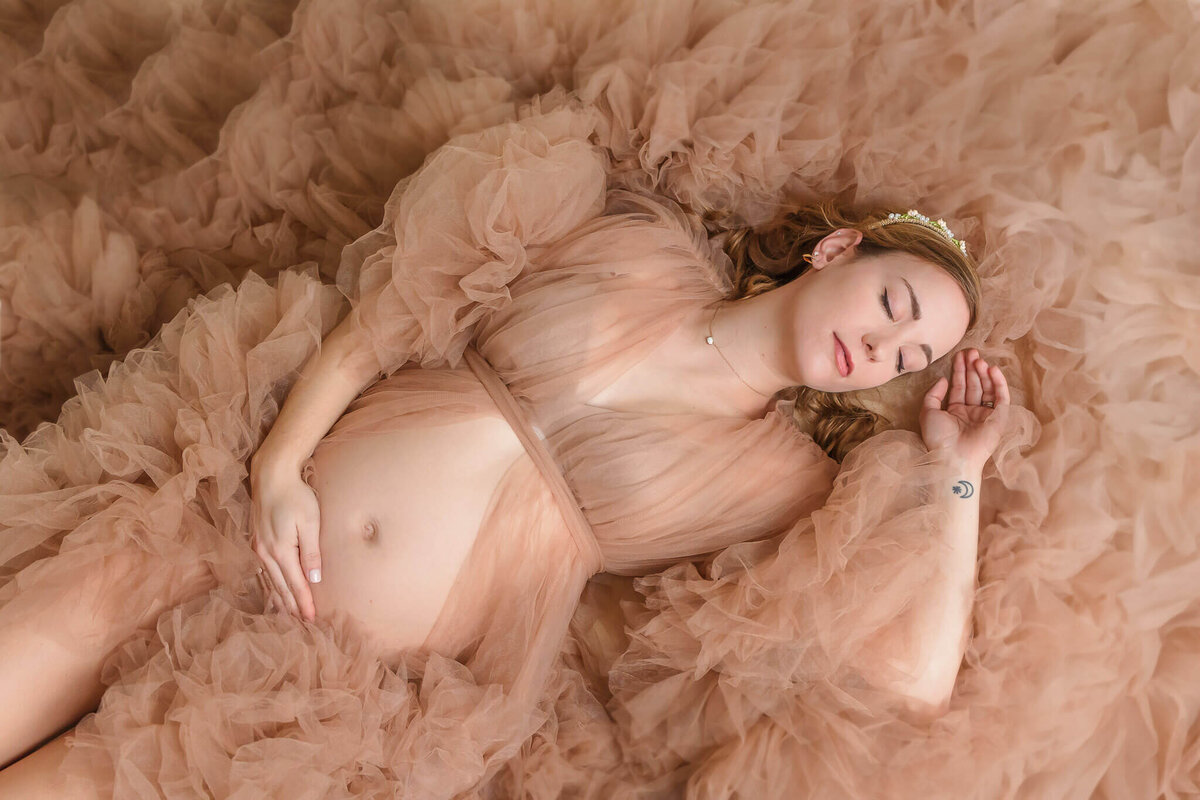A pregnant Northern VA woman laying down surrounded by her fluffy tan robe at a studio photography session.