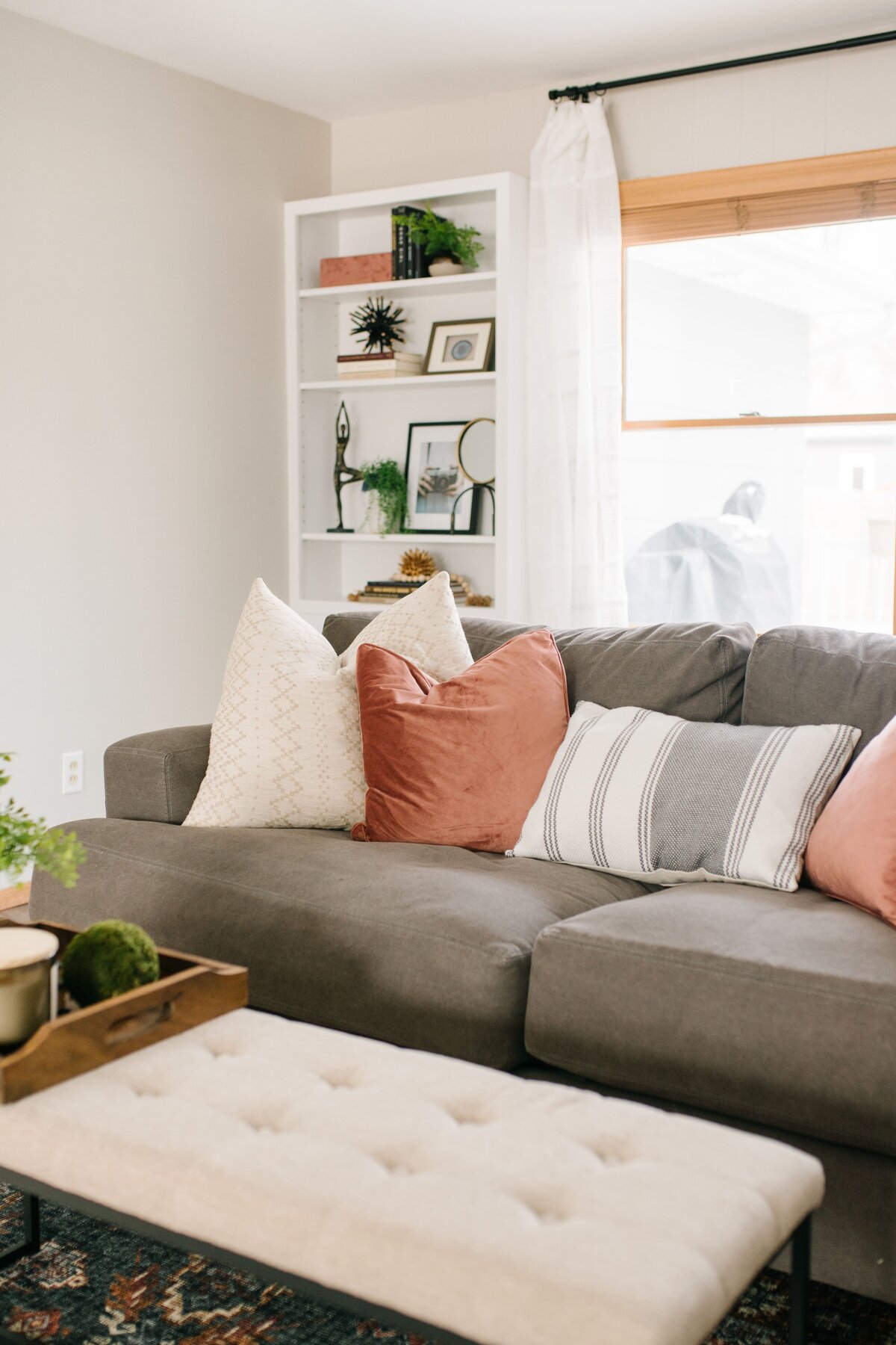 Pink and white pillows sit on a grey couch in a bright living room