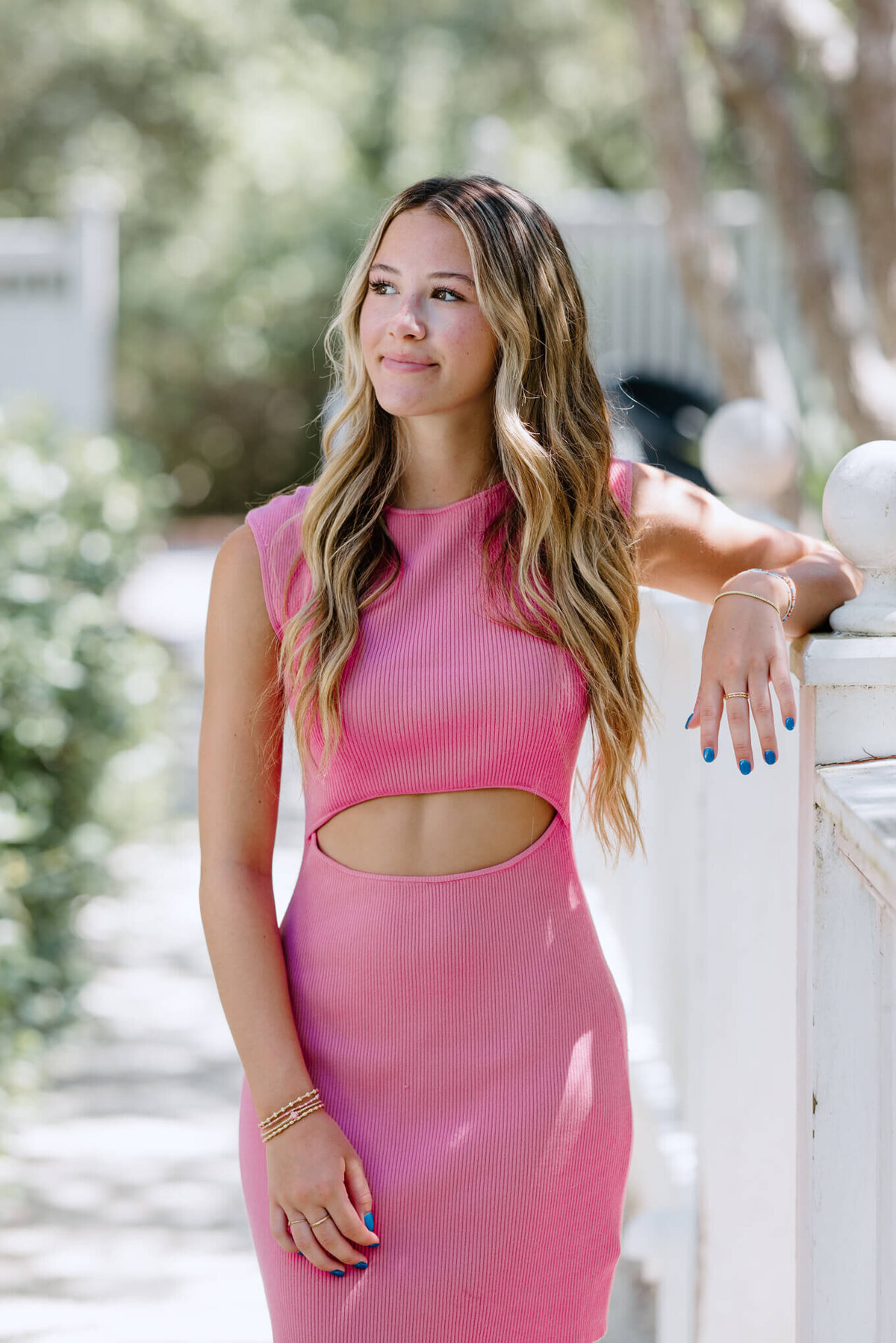 senior girl in light pink dress leaning on white picket fence