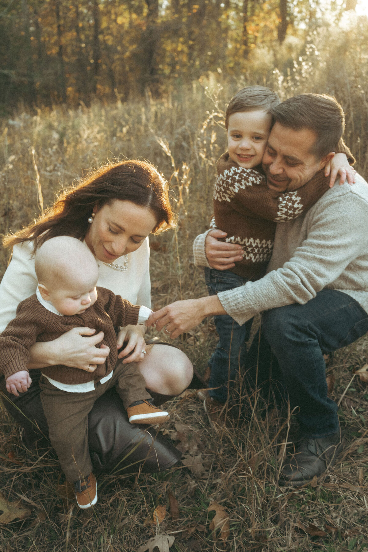 A mom and dad hold their two boys in a Hyde Farm Park field at golden hour. 