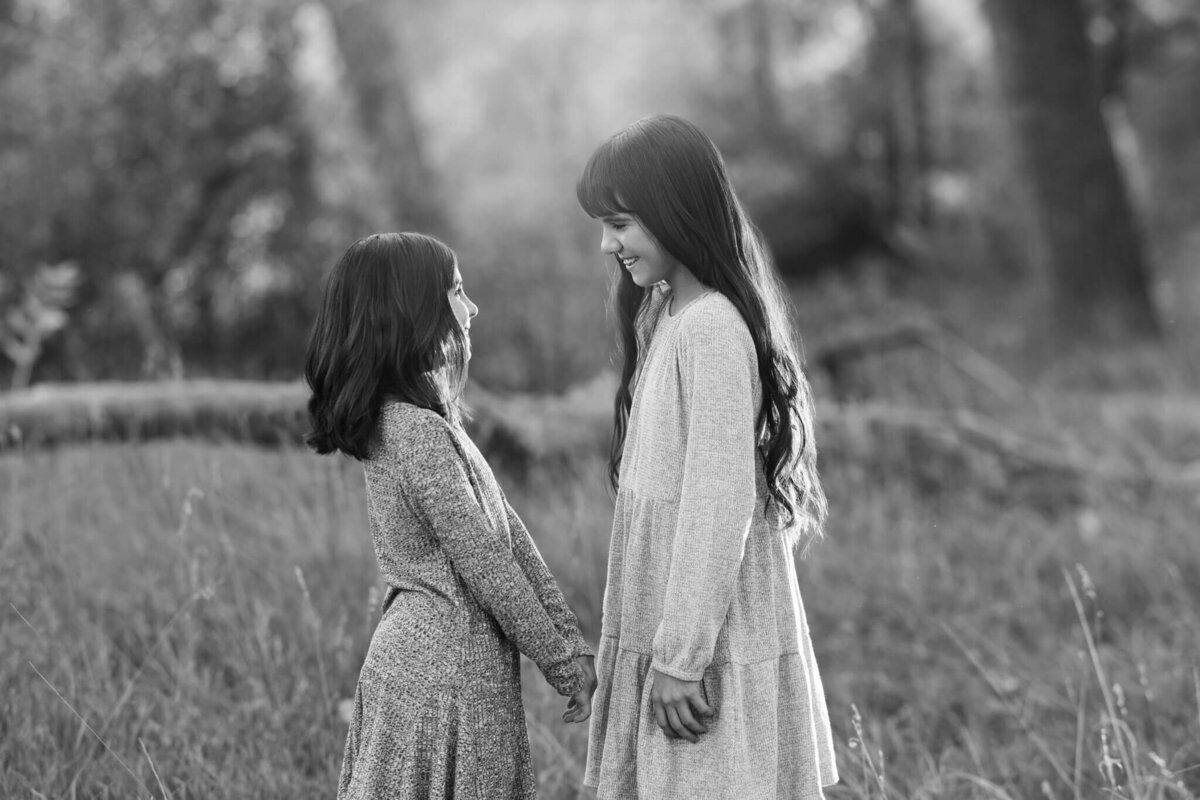 tow sisters holding hands looking at each other standing in a field