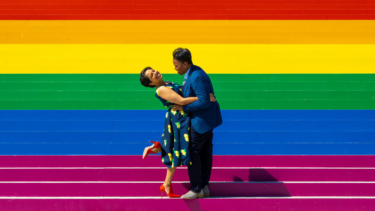 A couple hugging and smiling on a rainbow staircase.