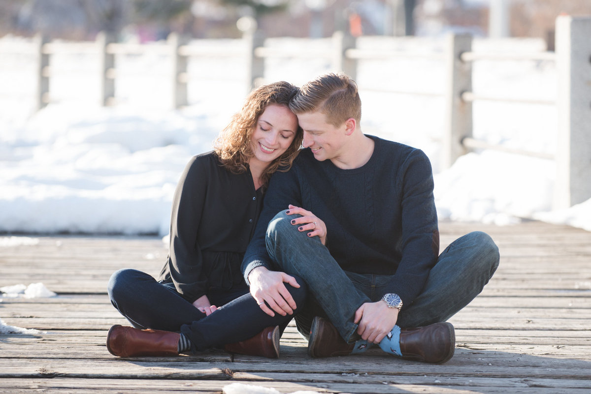 Engaged couple sitting on the dock of Dow's Lake during winter engagement session