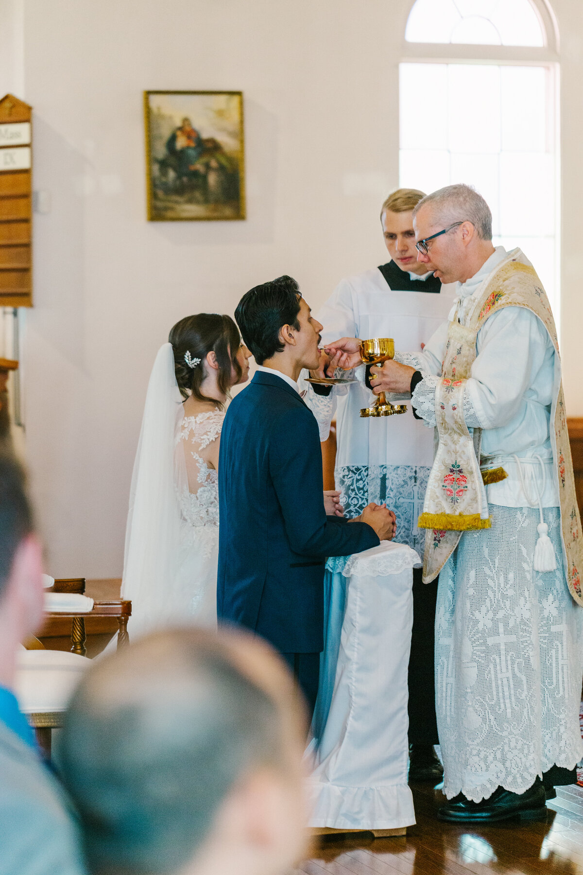 Bride and groom kneeling down taking communion from priest