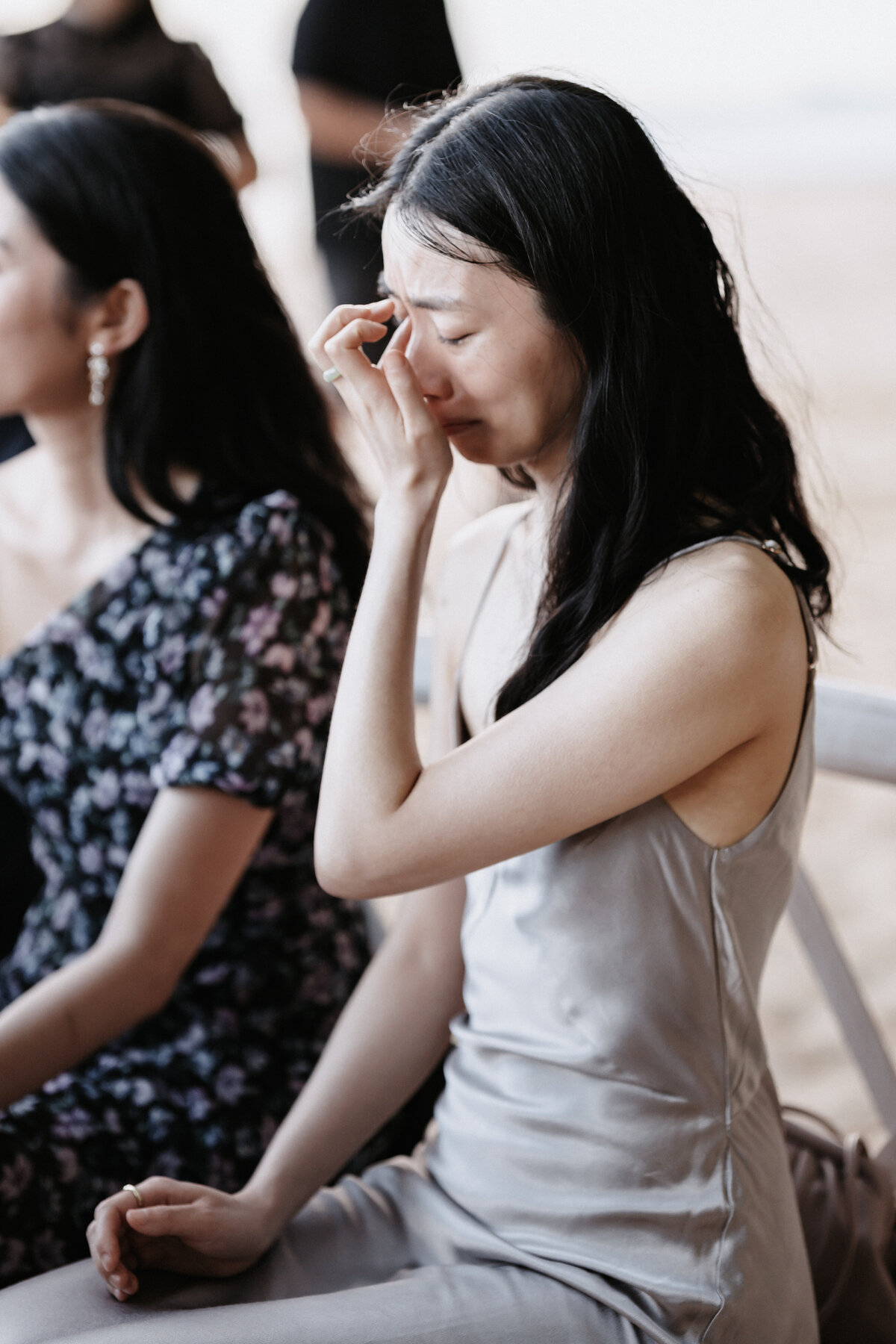 Wedding guest emotionally wiping tear wearing champagne dress during wedding ceremony