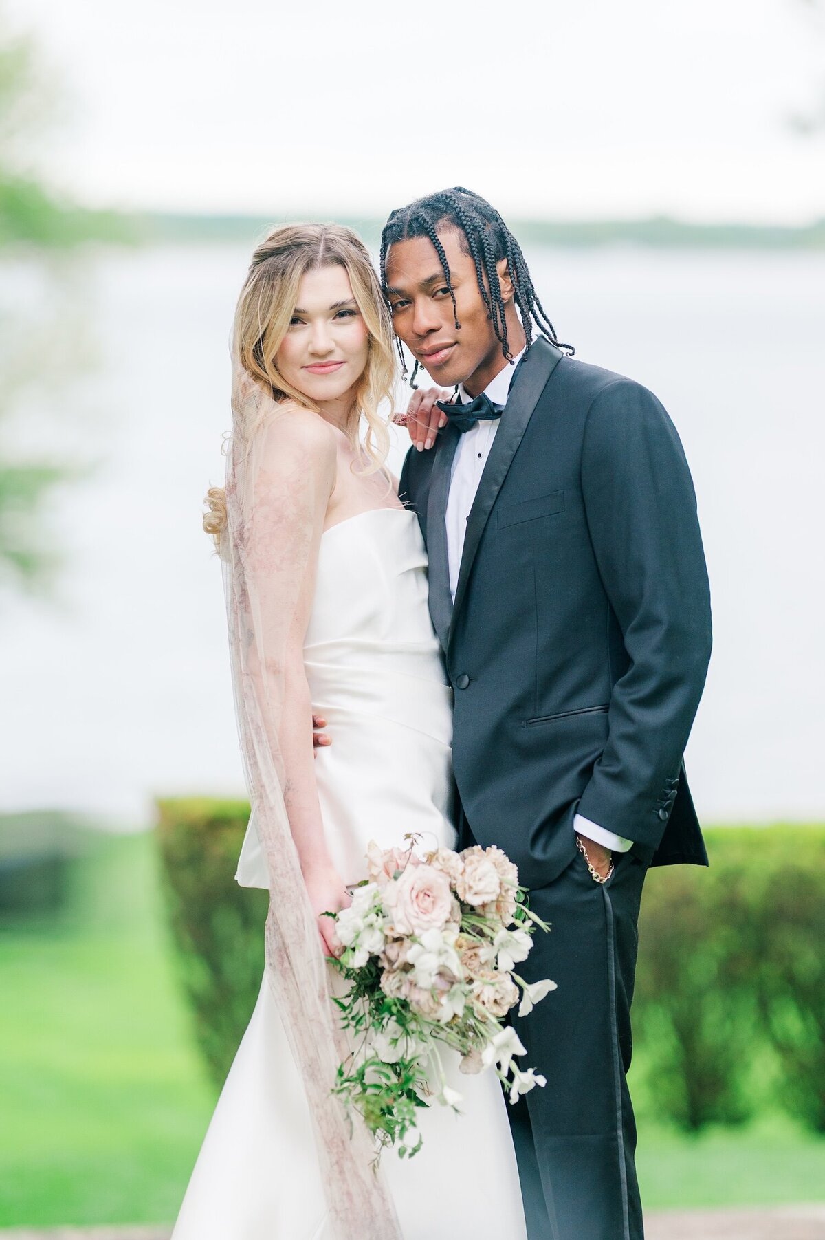 A bride and groom touching heads with the water outside of Glen Manor House in the background. 