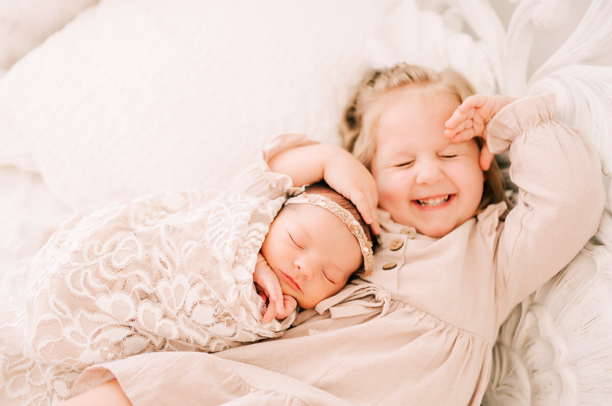 toddler girl and newborn uddling and smiling on bed captured by Springfield MO newborn photographer Jessica Kennedy of The XO Photography