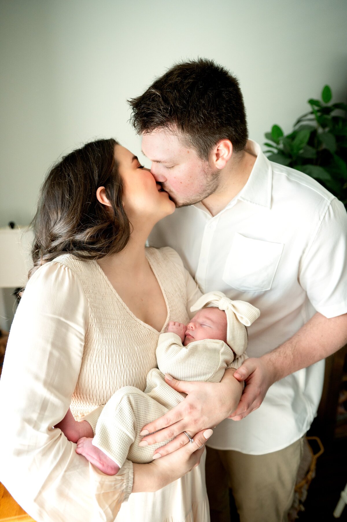 mom and dad kissing while they hold their baby