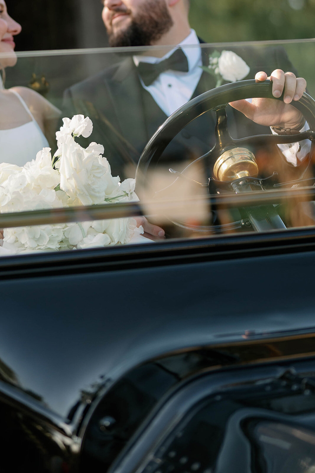 Newlyweds sitting together inside a vintage black car at Dearborn Village after their Martha-Mary Chapel ceremony.