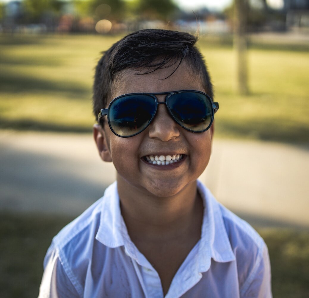 A little boy in a white collared shirt and sunglasses smiling