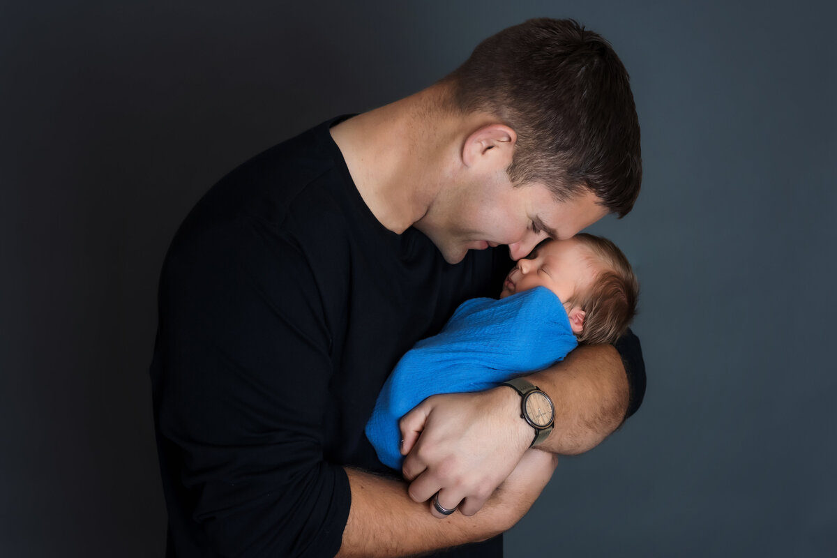 Newborn Photographer, a father smiles as he holds and admires  his baby