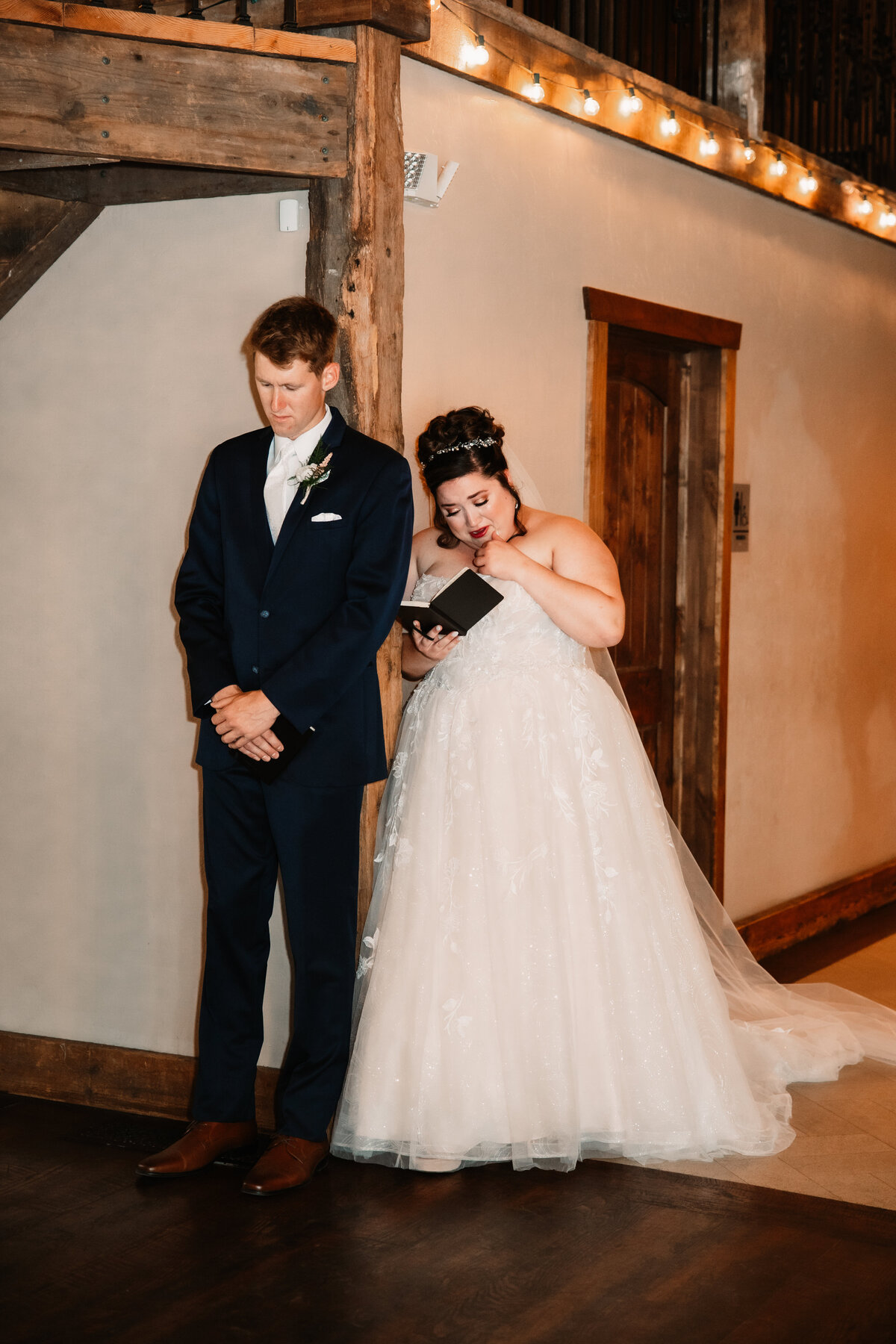 A bride leans on a wall reading her note with her groom facing away during first touch