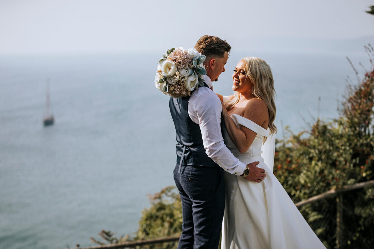 Bride and Groom embracing while standing on a cliff overlooking the sea