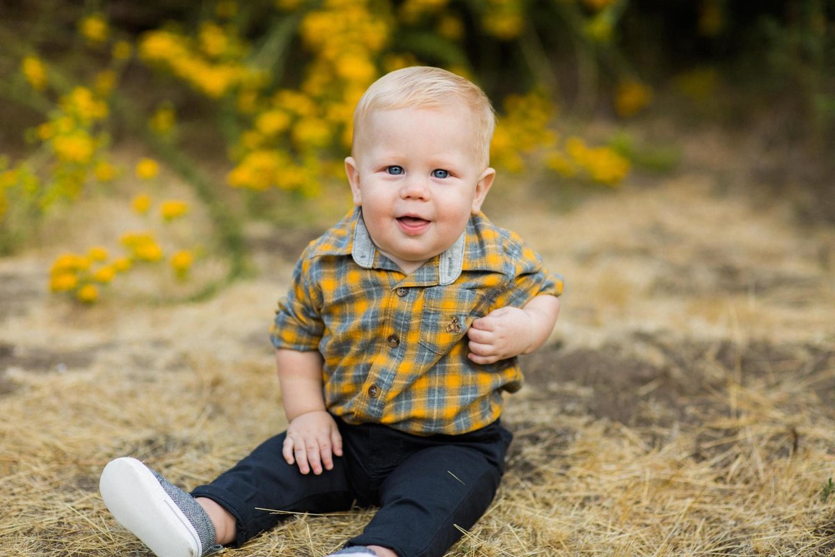 Little boy sits on the ground and smiles during family photo session