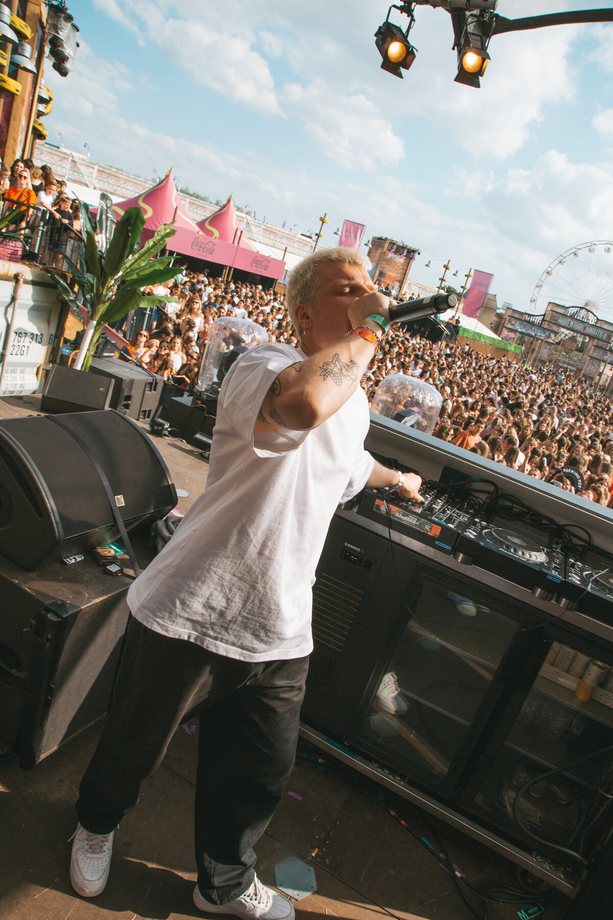 A high-energy club scene with Sam Hofman at the center of a crowded DJ booth, surrounded by enthusiastic fans reaching out towards him. The intense lighting and lively crowd emphasize the electric atmosphere. Photographed by Bo Eppink.
