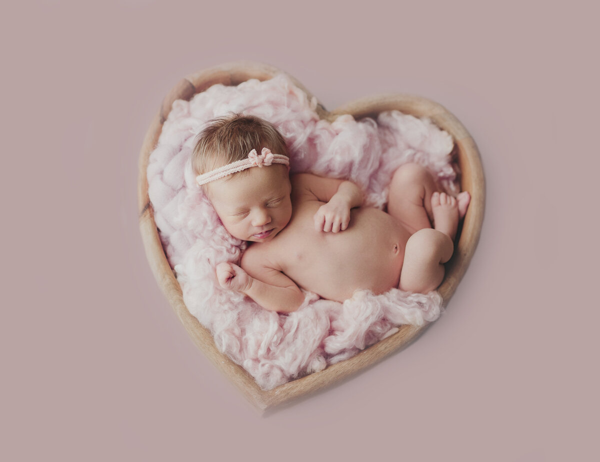 baby laying in pink heart basket