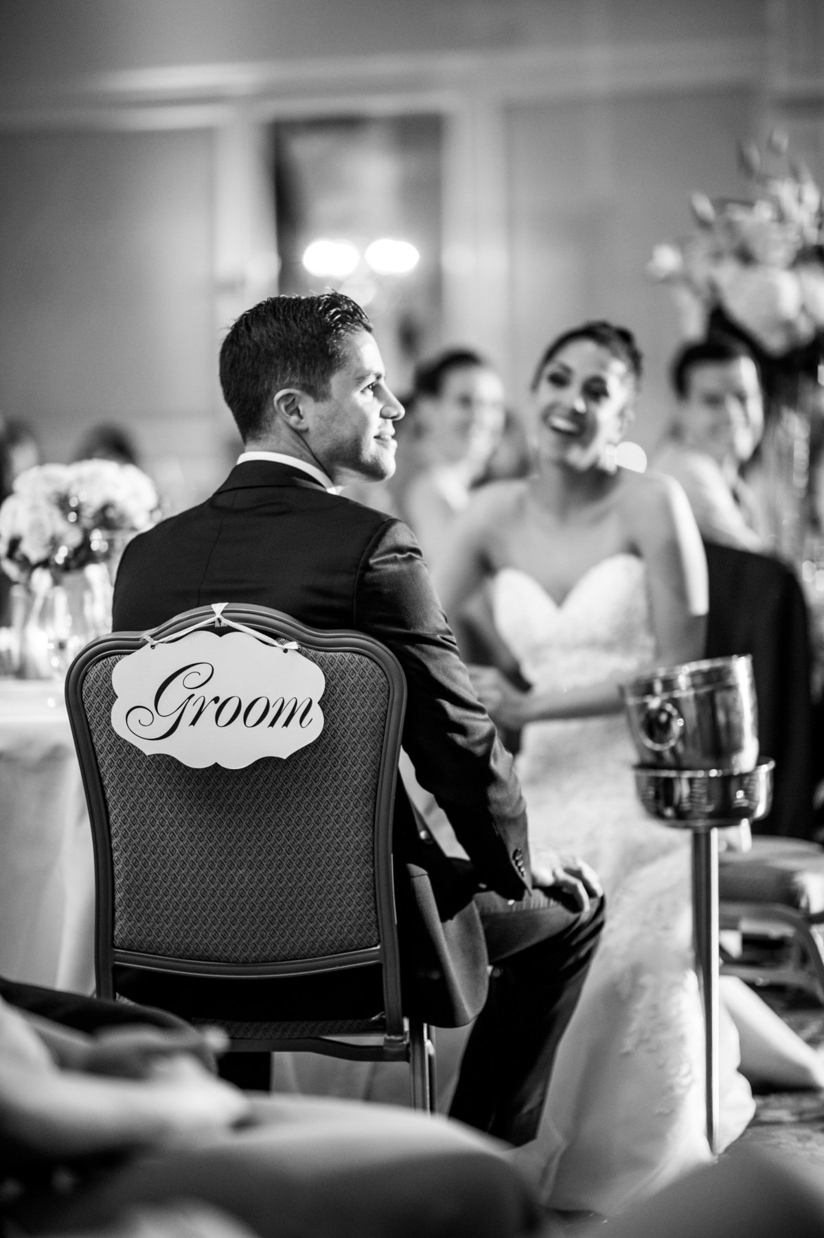 Groom sitting in his chair at the reception with a Groom sign hanging from the back.