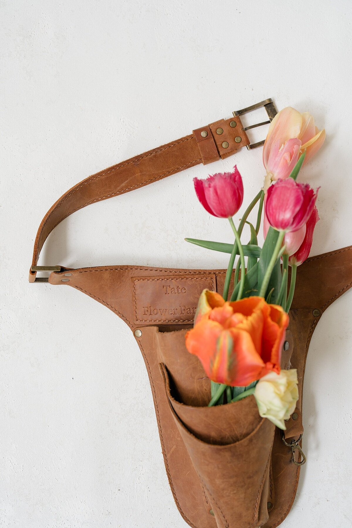 branding photography for a florist with flowers stuffed into a pocket of a gardening belt