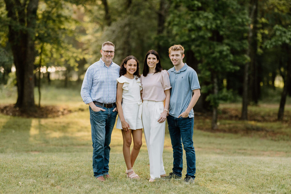Spring time family portrait of Longview, TX family wearing neutral colors  while standing in an open landscaped field