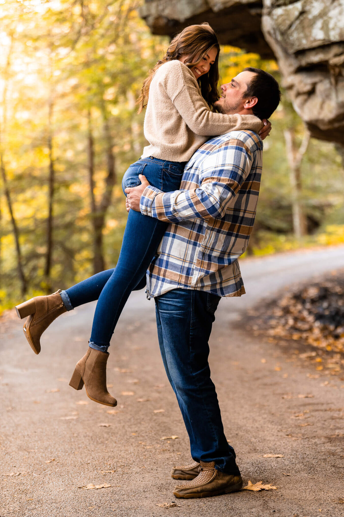 Man lifting his fiance while they smile together on a gravel road in McConnell's Mill State Park. Captured near sunset near portersville, PA by Pittsburgh engagement photographer Michael Fricke Photography