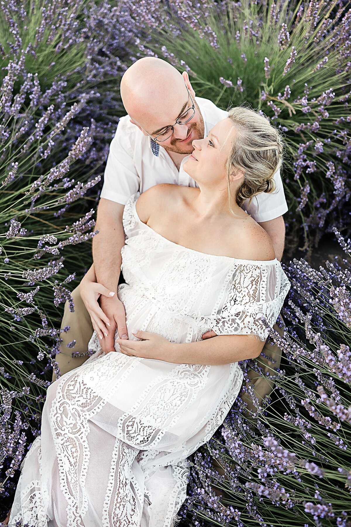 husband and wife laying in lavendar field for maternity photo session