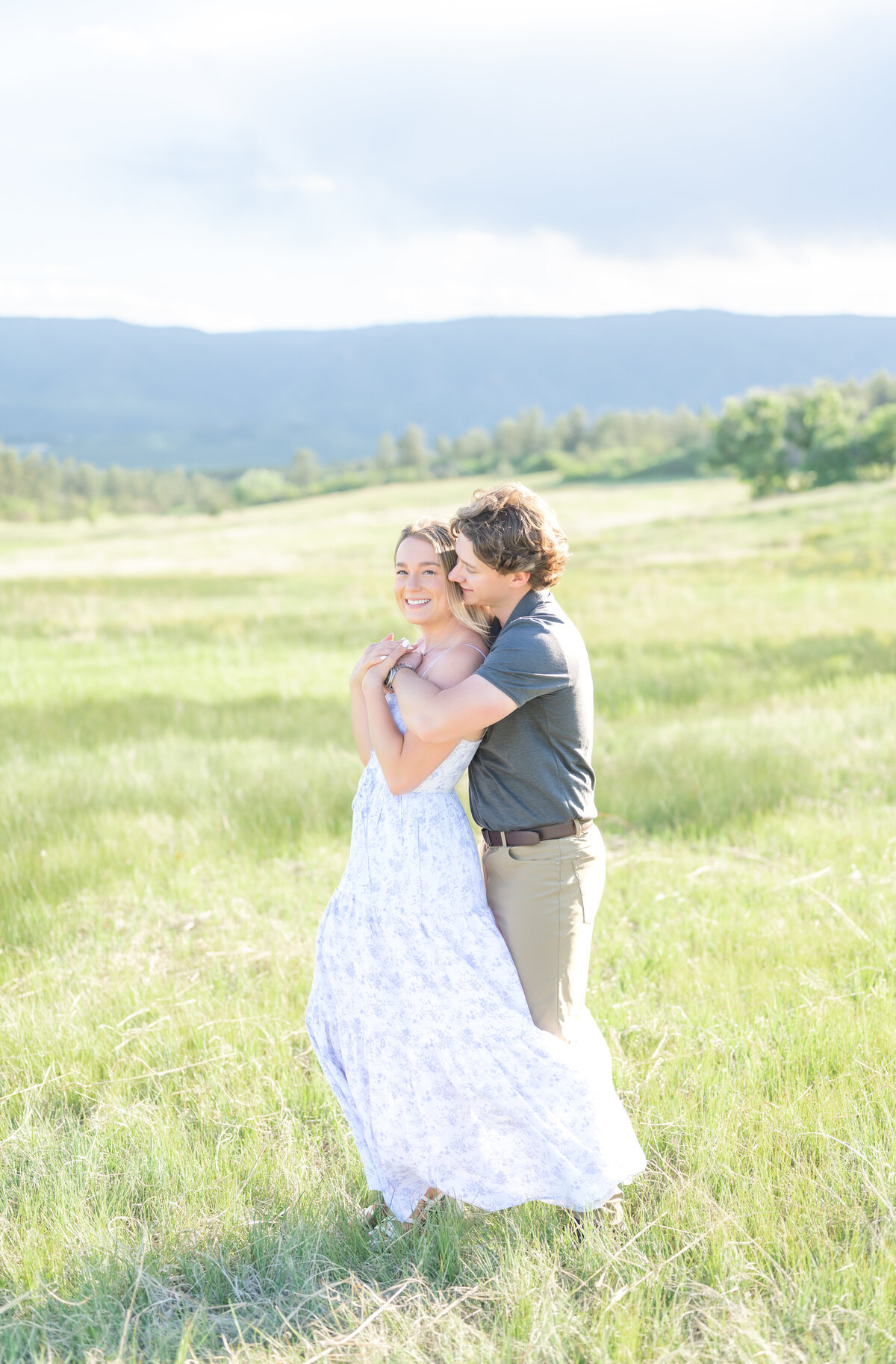 Boy giving his fiance an intimate bear hug while smiling and looking at her in an open field