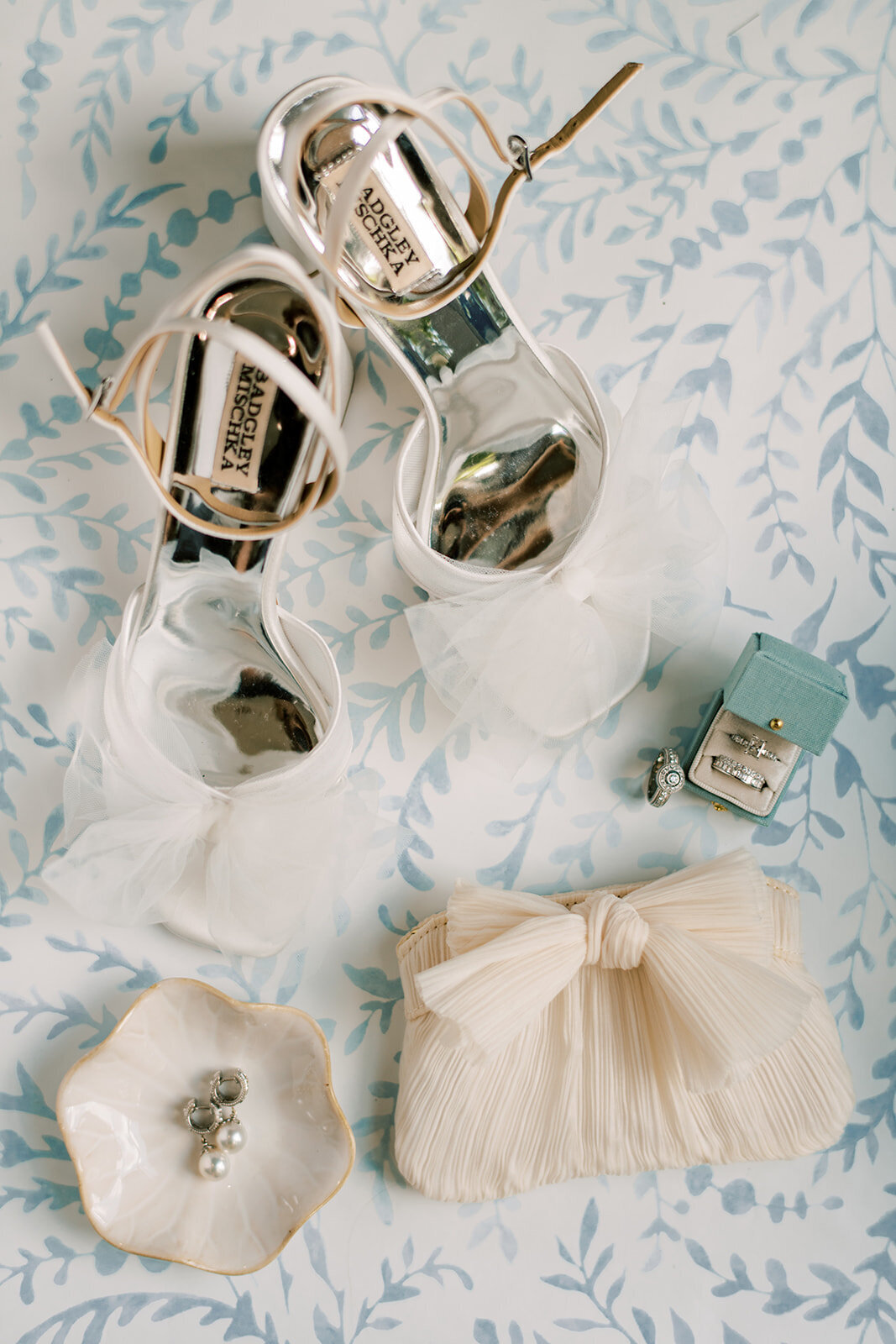  Bridal accessories including white heels, clutch, and ring box styled in a soft blue flatlay for a Cashiers NC wedding.