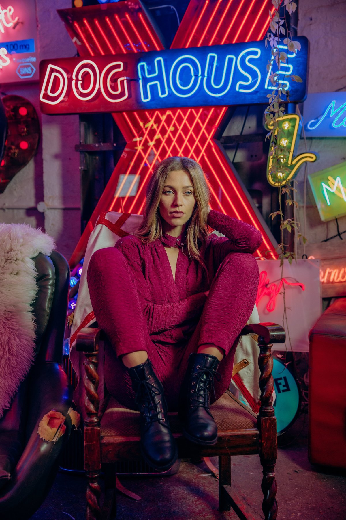 Anastazja sat in a chair, wearing a pink jumpsuit infront of an X shaped neon sign