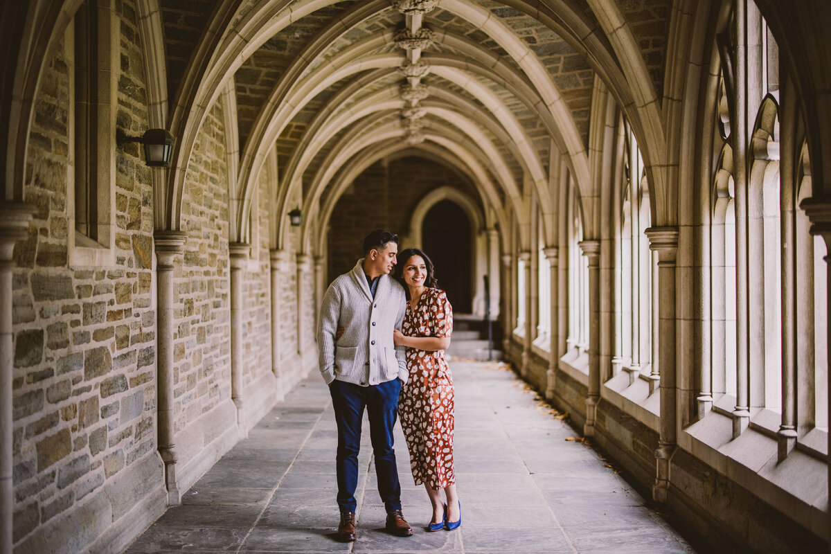 Engaged couple looking through window in a gothic hallway at Princeton University in NJ