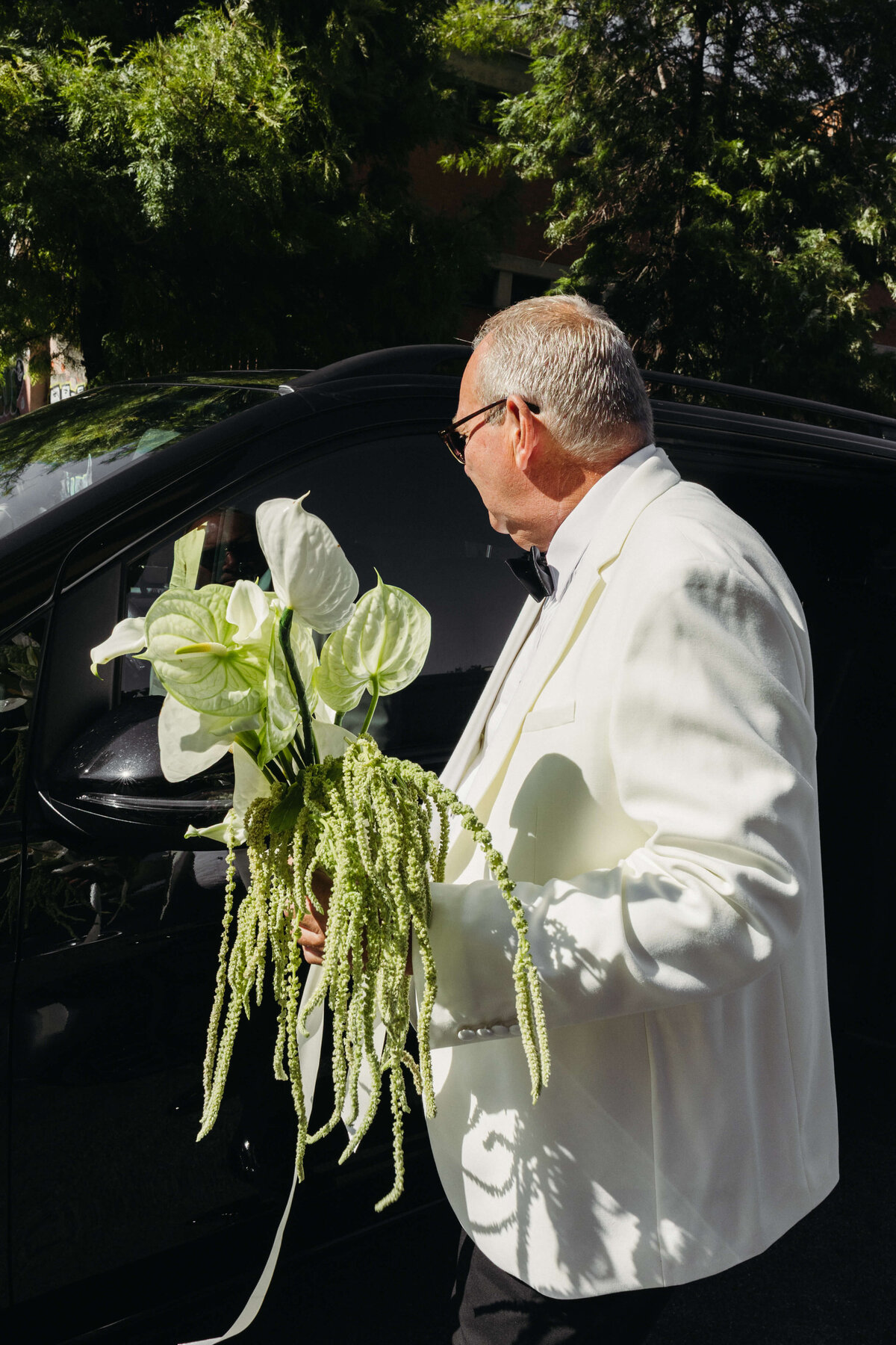 Father of the bride holding modern tropical bouquet outside black car

