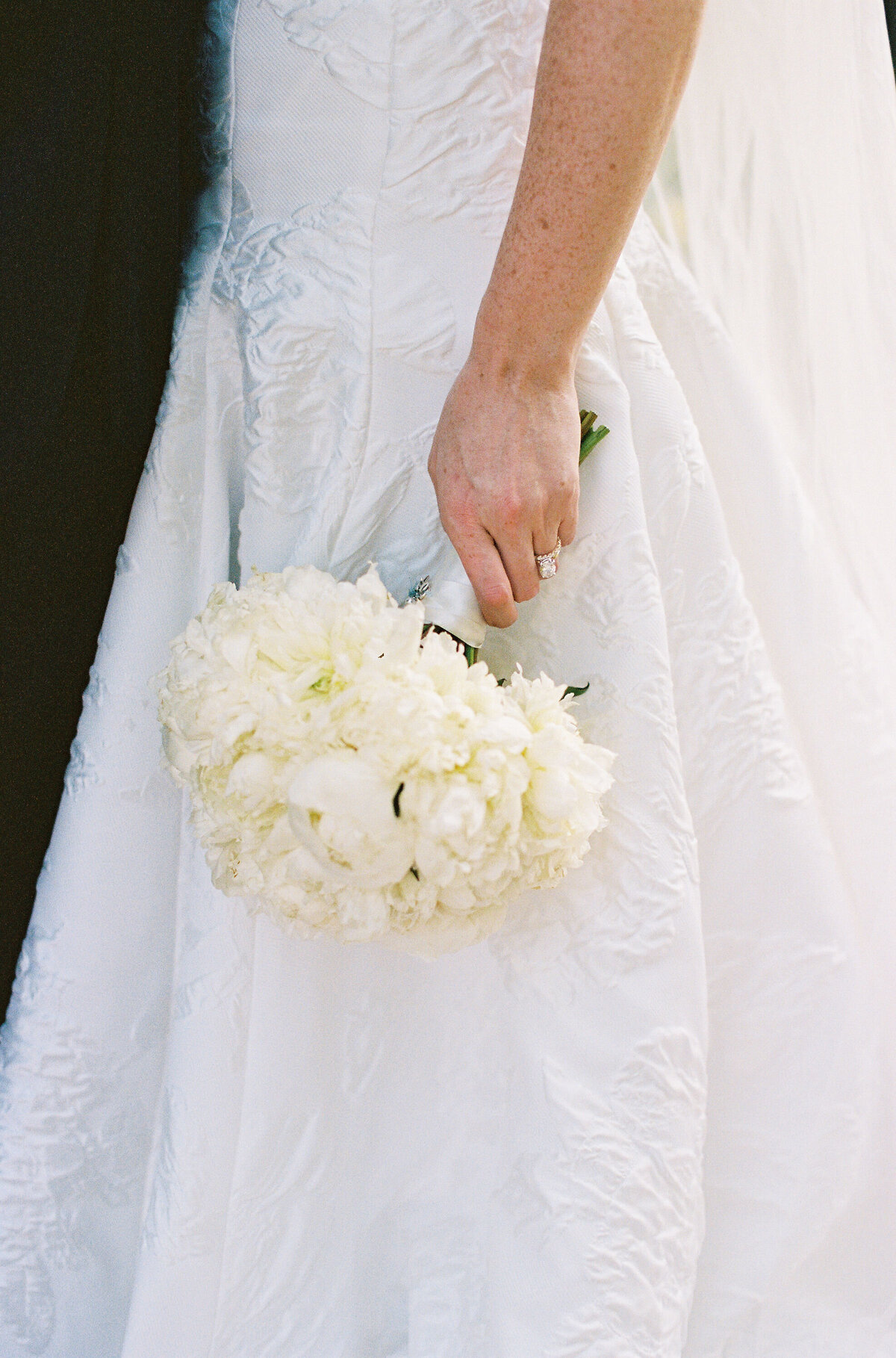Close-up of the bride holding a white floral bouquet.