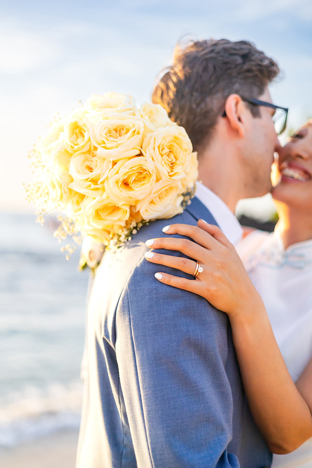 bride and groom laughing and holding eachother at the beach showing wedding ring  and yellow bouquet