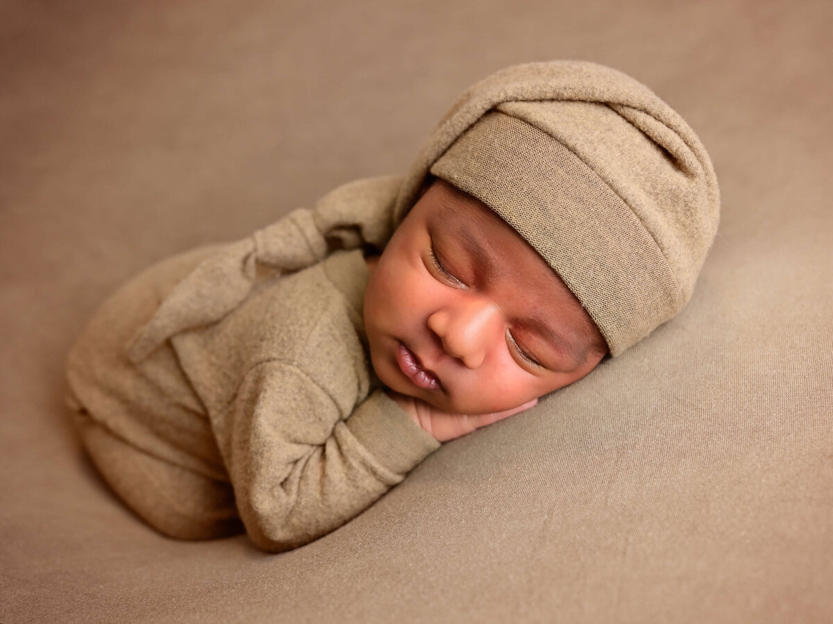 Newborn photoshoot in Kitsap County, WA captured by Beth Benecki.  Newborn posed sleeping on his belly with hands under his cheek. Baby dressed in tan outfit with matching sleepy cap.