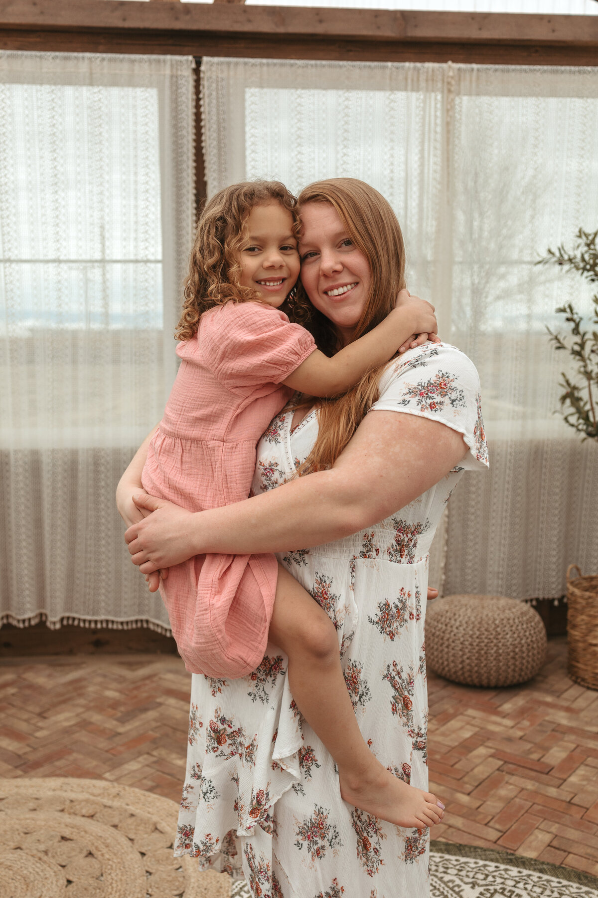 mom holding daughter in pink dress while they're both looking at the camera smiling in longmont colorado during family session with alexis adkins photography