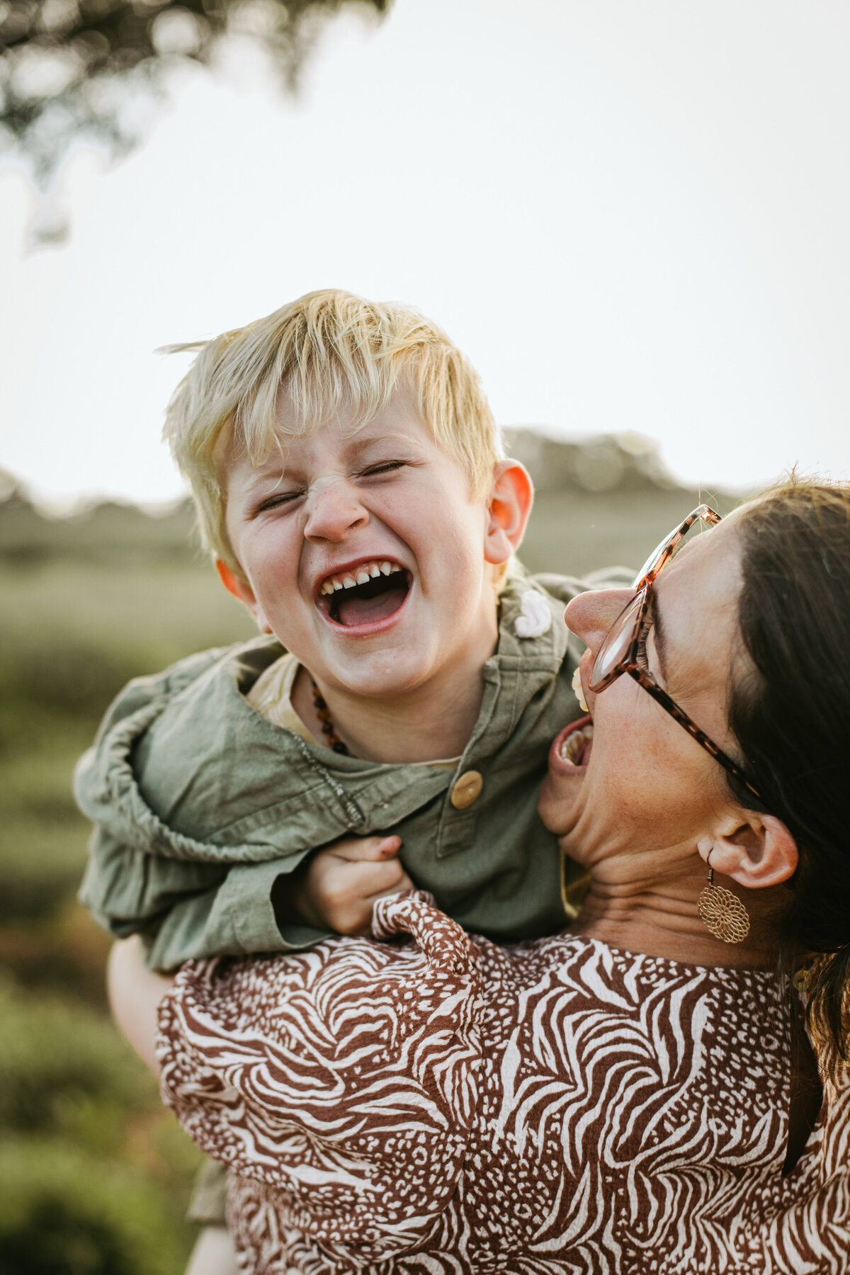 Mother shares a playful moment, holding her son and tickling him as he laughs with eyes shut.