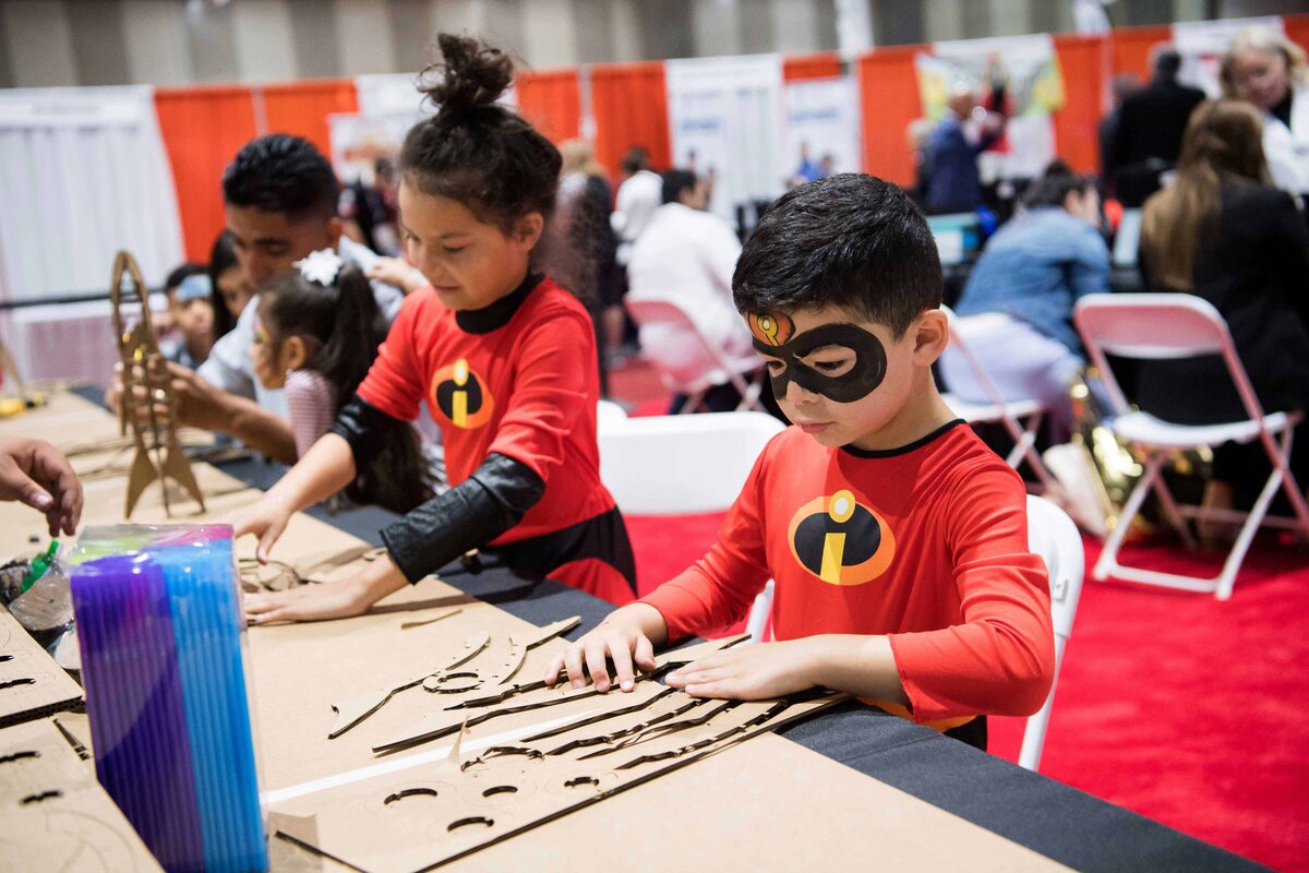 4 young children assemble a rocket at a conference booth in San Diego .  They are dressed in costume