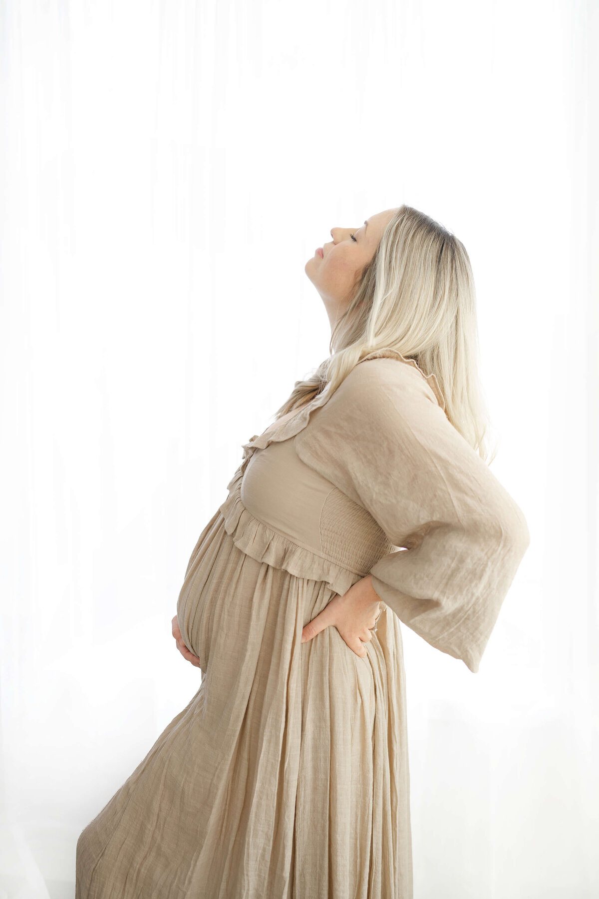 gorgeous mother to be looking up as she supports her back in a natural light photography studio