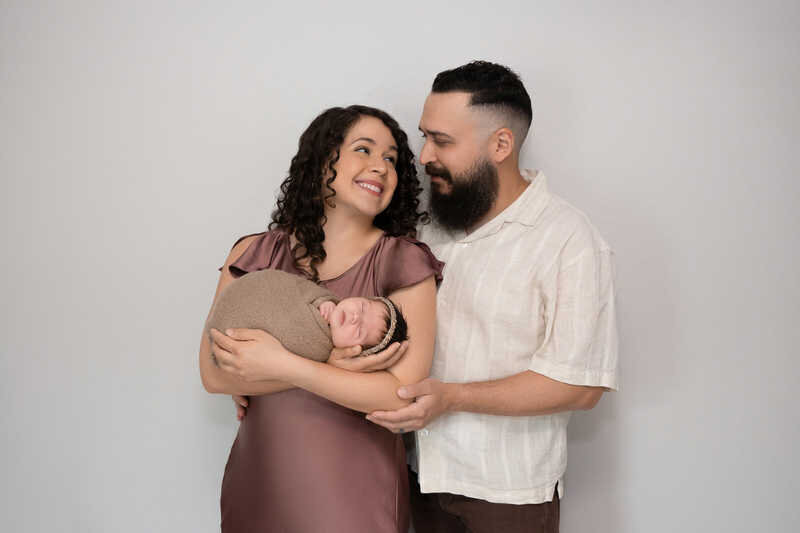Parents smiling together while holding their newborn during Houston family portraits.