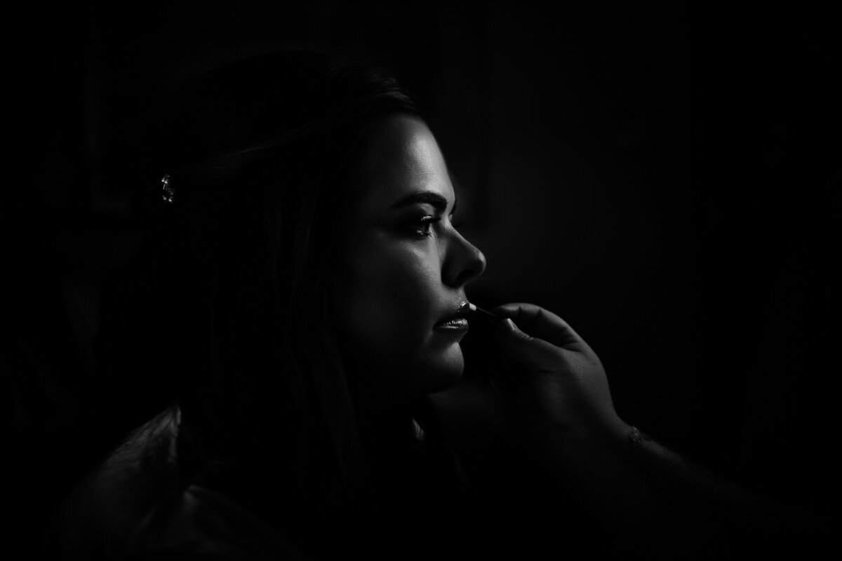 bride having finishing touch makeup on her lips in black and white photography