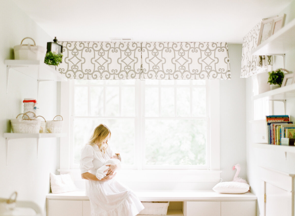 Mom holds her newborn daughter while sitting in a window seat. Image by Raleigh newborn photographer A.J. Dunlap Photography.