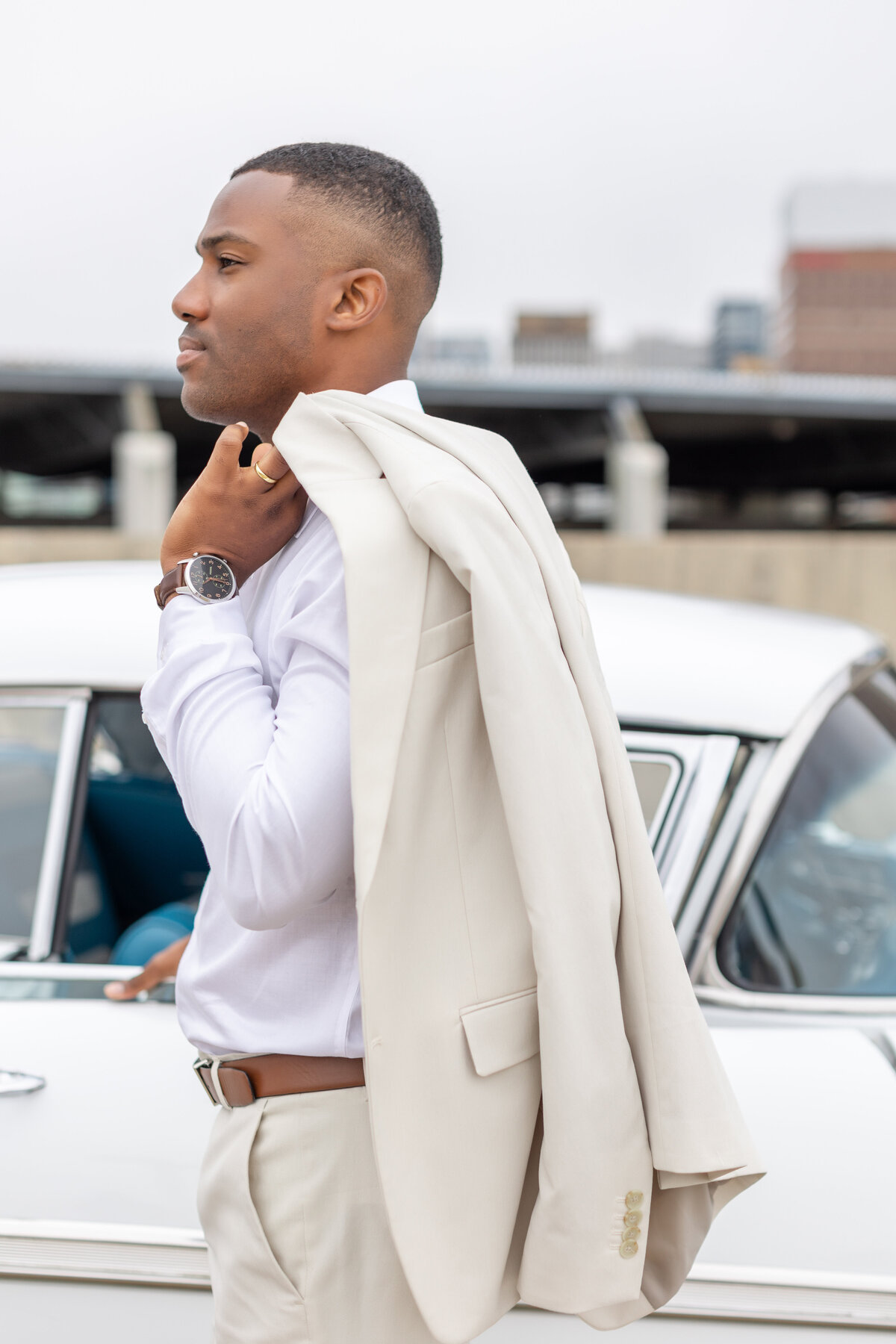 Groom posing with cream colored jacket on rooftop in Halifax